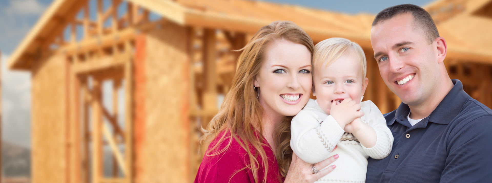Family holding baby in front of house construction site